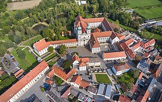 Luftaufnahme der Stiftsbasilika Waldsassen mit dem weitläufigen Klosterkomplex, umgeben von roten Dächern, einem großen Platz und grünen Parkanlagen.