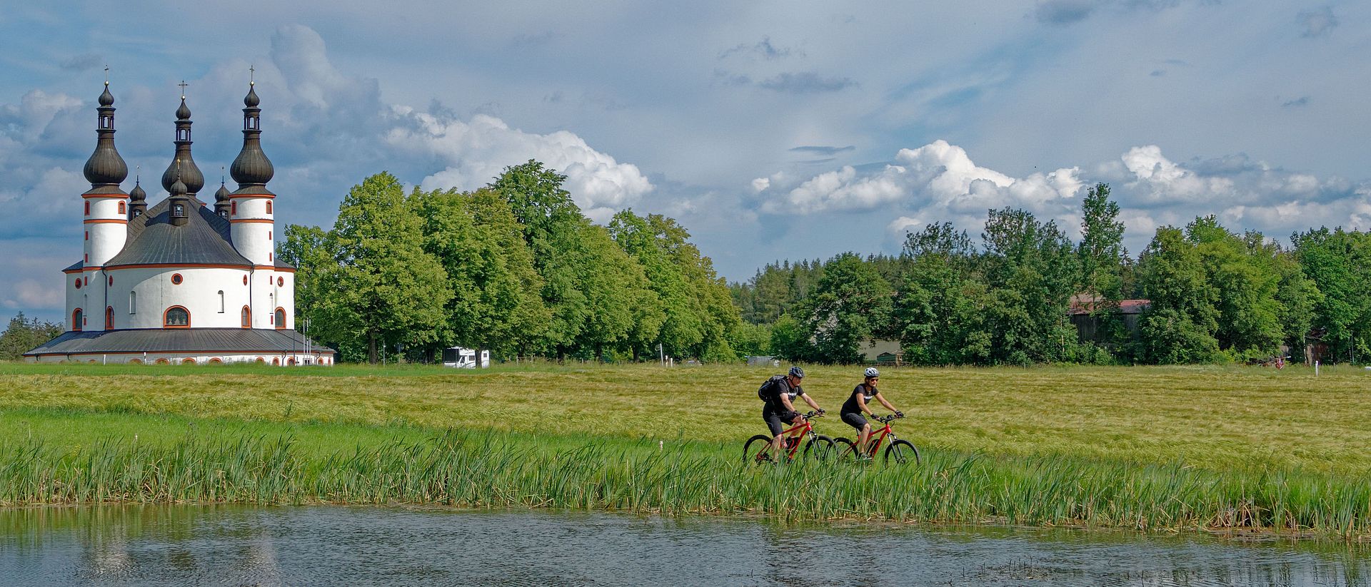 Zwei Fahrradfahrer auf einer Wiese mit Kappl im Hintergrund.