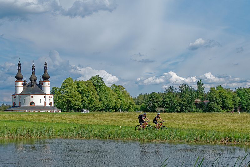 Zwei Fahrradfahrer auf einer Wiese mit Kappl im Hintergrund.